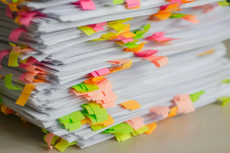 Piles de dossiers papier annotés de notes adhésives, en attente de traitement