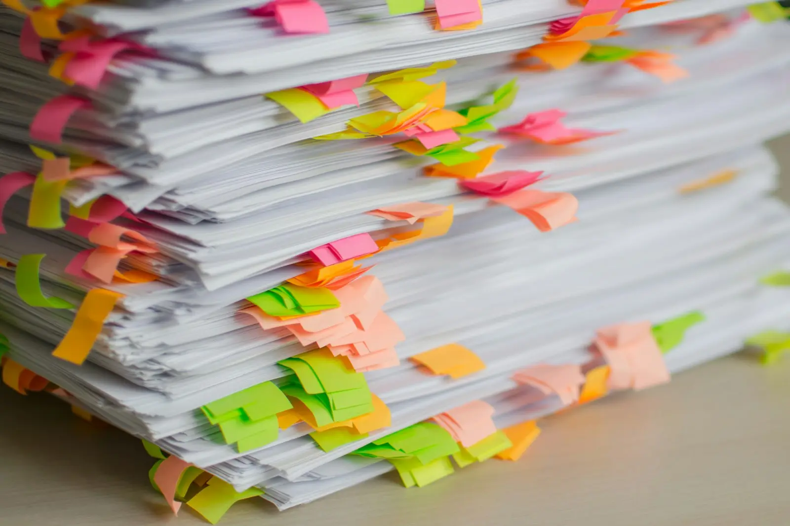 Piles de dossiers papier annotés de notes adhésives, en attente de traitement